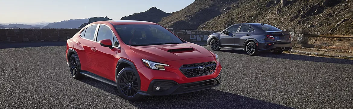 Red and blue Subaru WRX sedans parked together on a mountain road