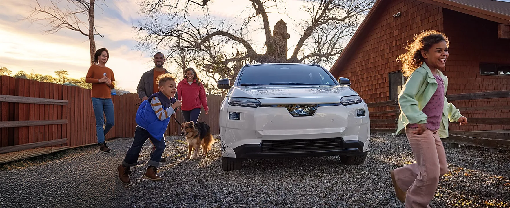 A family in a driveway beside a white 2026 Subaru Solterra as a child runs past