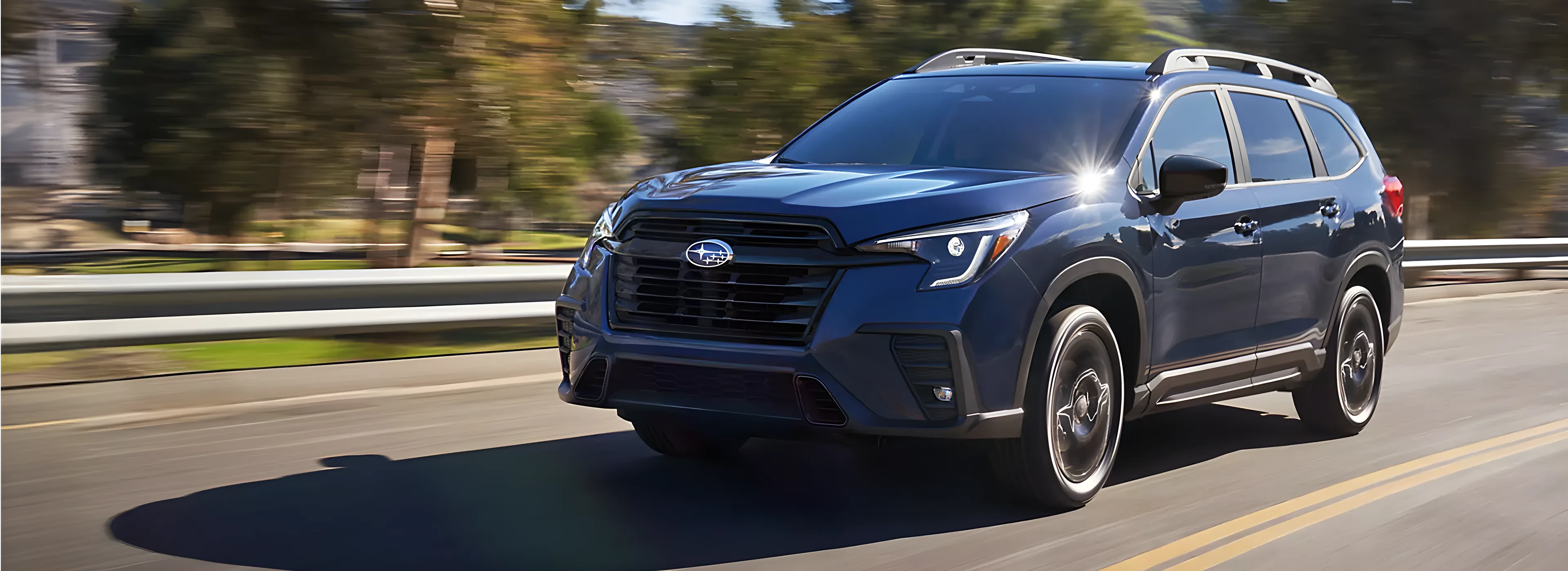 A dark blue 2026 Subaru Ascent driving on a sunlit highway past rolling hills