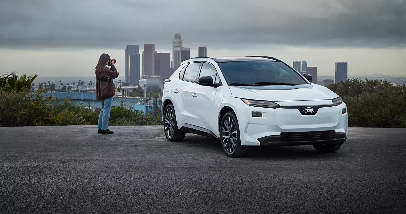 A white 2026 Subaru Solterra parked on a hill overlooking a city skyline