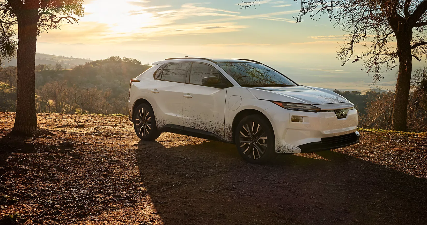 A white 2026 Subaru Solterra parked in an open field at sunset