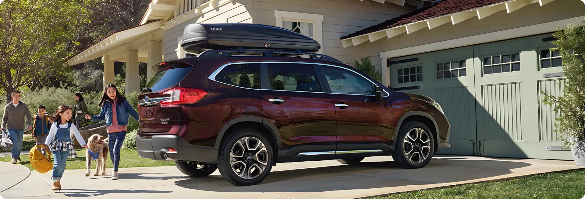 A dark red 2026 Subaru Ascent parked in a driveway as a family loads it for a trip