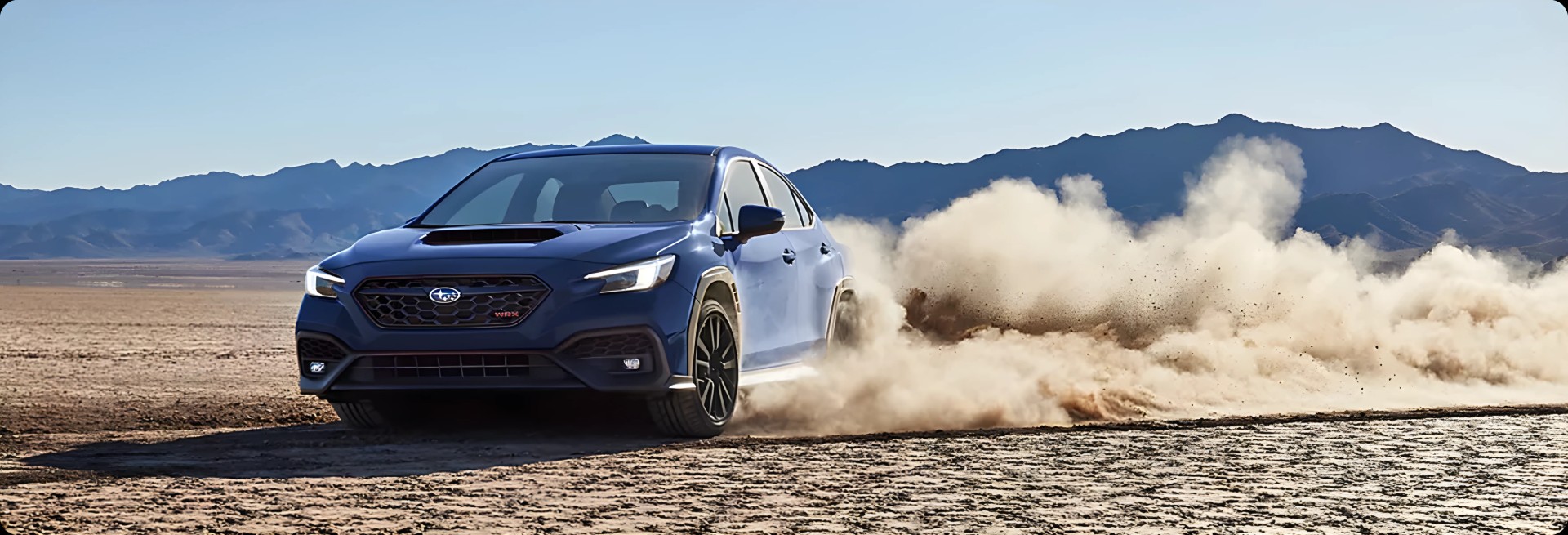 A blue Subaru WRX kicking up dust across an open desert flat