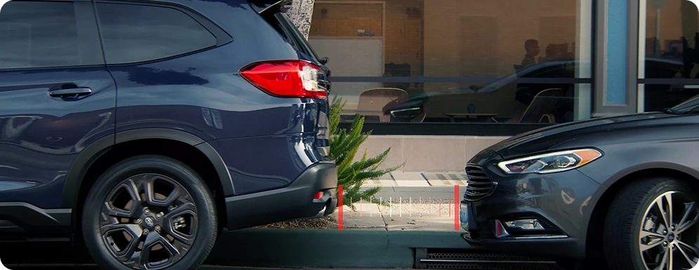 A dark blue Subaru SUV reversing toward a parked sedan with red proximity markers on the pavement between them