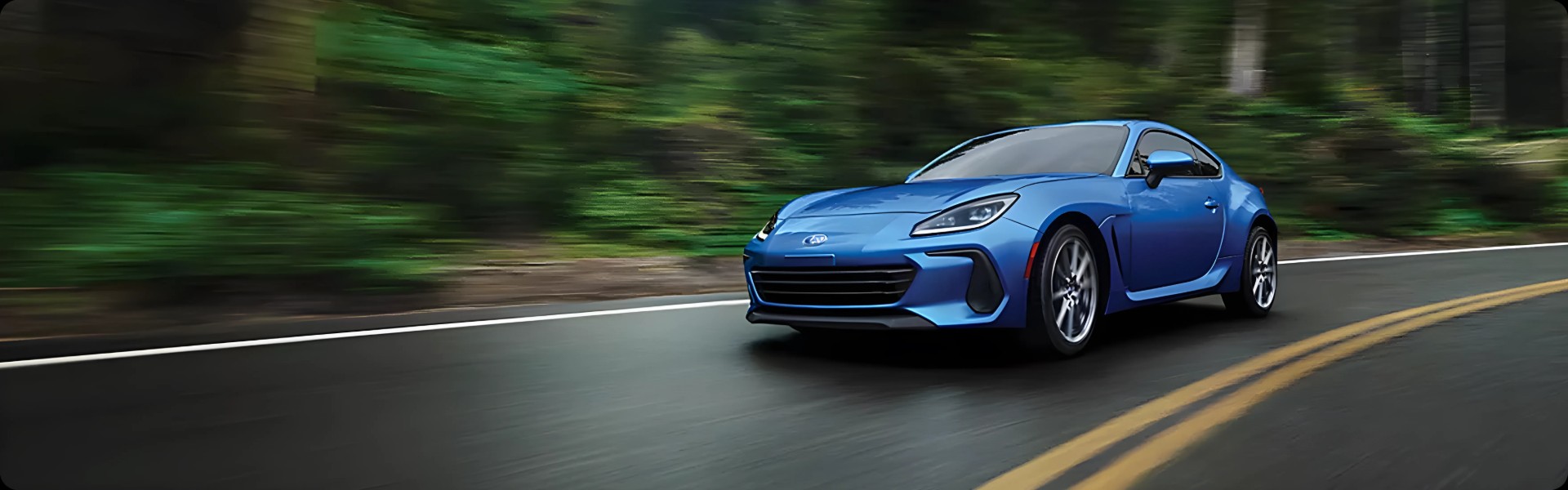 A blue Subaru BRZ on a winding forest road