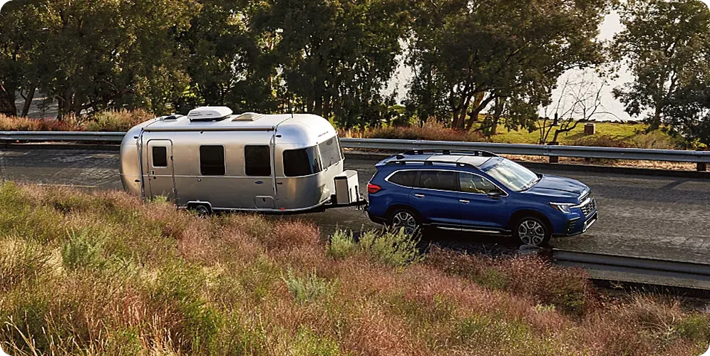 A blue Subaru Ascent towing a silver Airstream trailer through open countryside