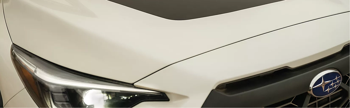 A close-up of the headlight, hood, and Subaru badge of a white Subaru Crosstrek