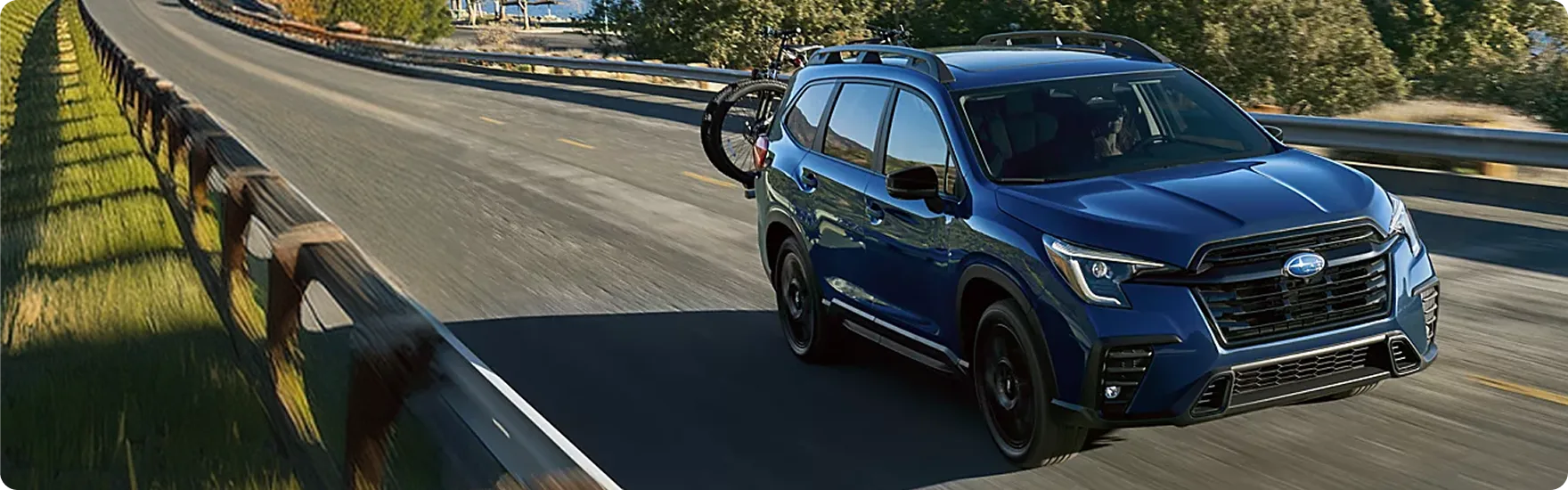 A blue Subaru Ascent travelling a coastal highway beside the water