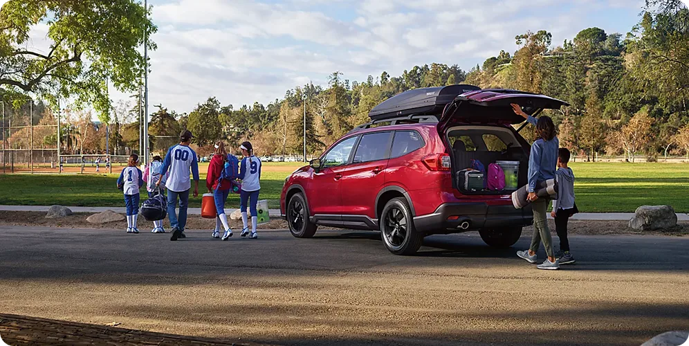 A family loading sports gear through the open power rear gate of a red Subaru Ascent