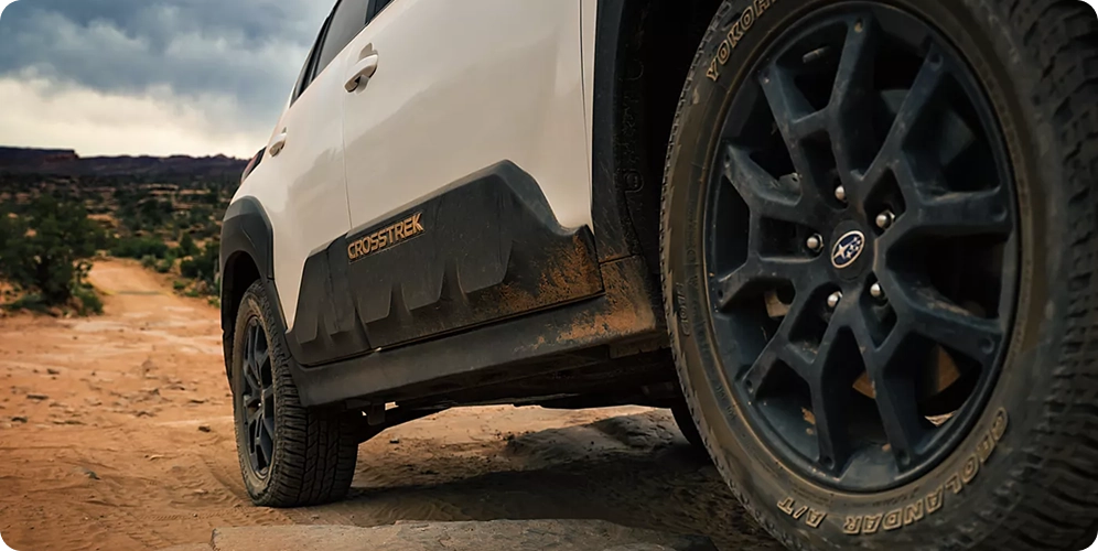 A close-up of the black wheel arch, all-terrain tire, and CROSSTREK badging of a white Subaru Crosstrek Wilderness on a desert trail