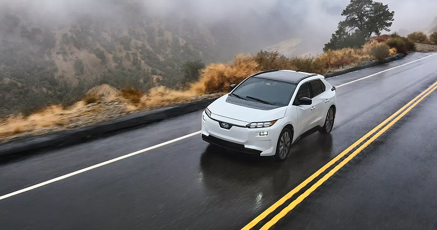 A white 2026 Subaru Solterra travelling a wet two-lane road