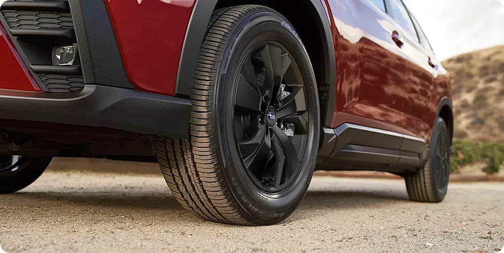 Close-up of a red Subaru Ascent front wheel and black alloy rim on rough ground