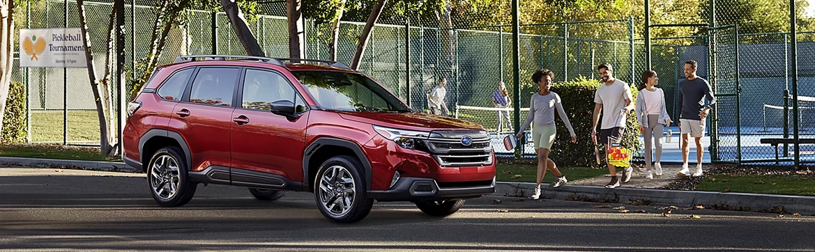 A red Subaru Forester parked beside a tennis court as a family walks past with sports gear