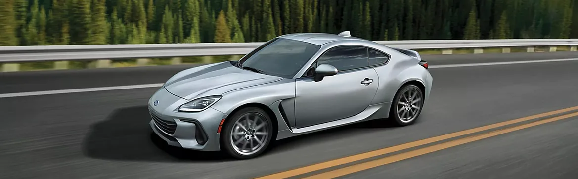 A silver Subaru BRZ on a mountain road lined with pines