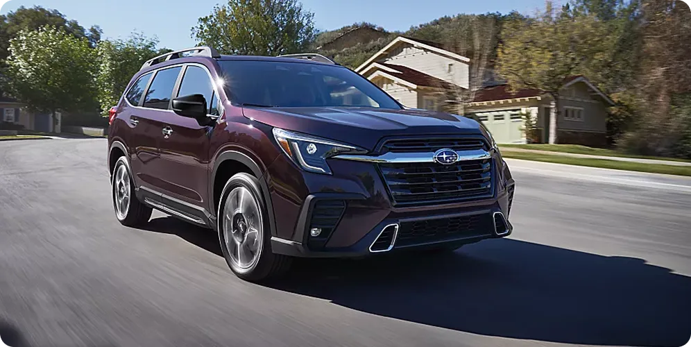 A dark Subaru Ascent accelerating along a suburban road