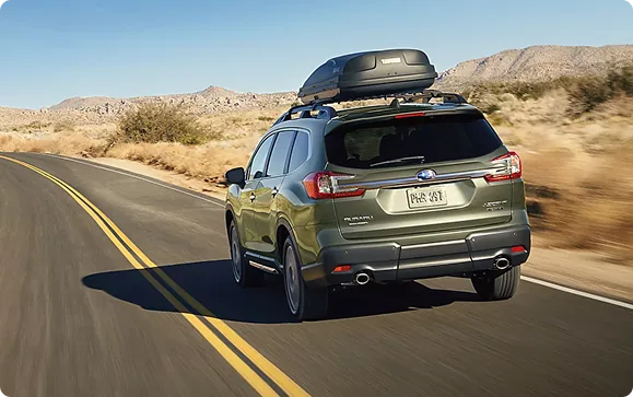 A green Subaru Ascent with a loaded roof rack on a desert highway