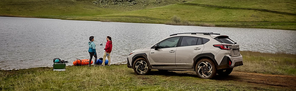 Two people setting up a picnic beside a champagne Subaru Crosstrek at a mountain lake