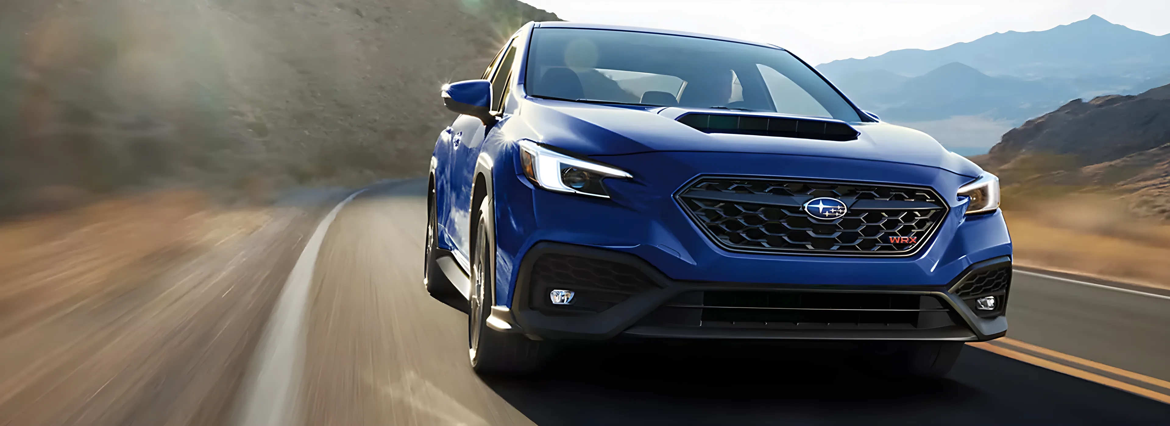 A blue 2026 Subaru WRX cornering on a sunlit mountain road