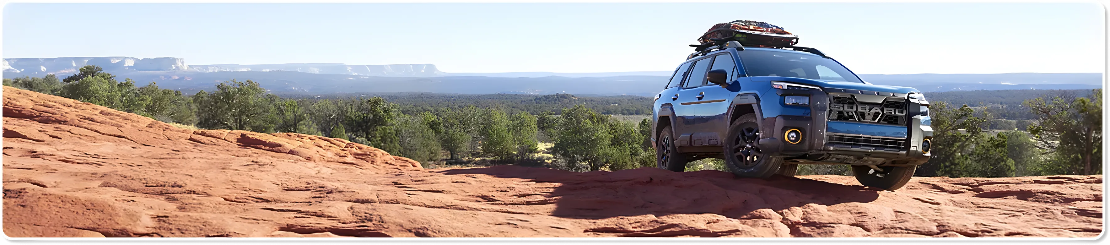 A blue Subaru Outback parked on red rock under a wide desert sky