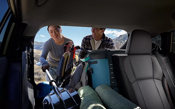 A couple loading duffel bags and coolers into the folded-flat cargo area of a Subaru Crosstrek