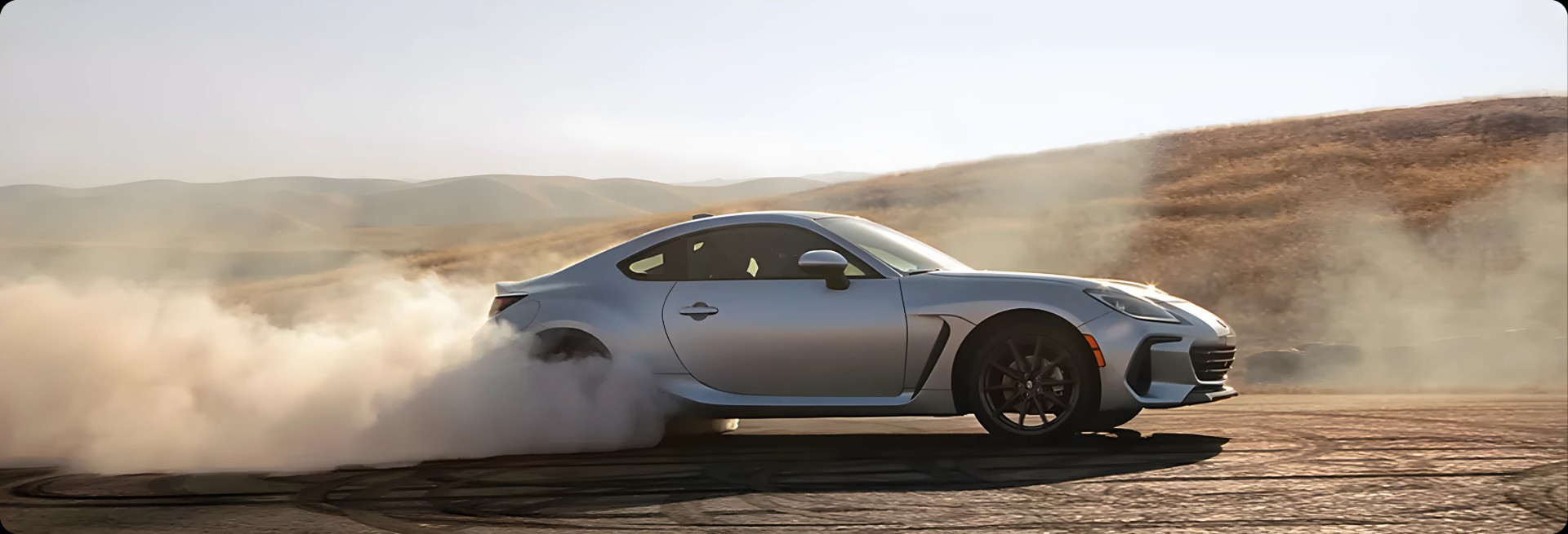 A grey Subaru BRZ kicking up dust through a sweeping turn
