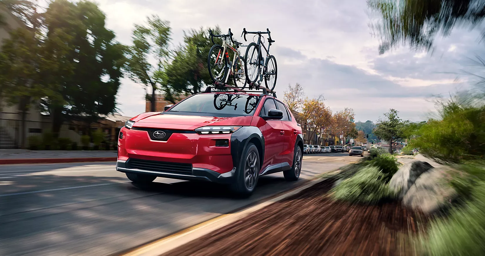 A red 2026 Subaru Solterra with bikes on the roof rack on a tree-lined street