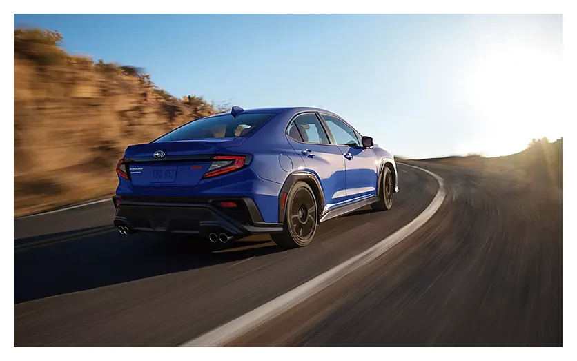 A blue Subaru WRX carving a mountain corner into the sun