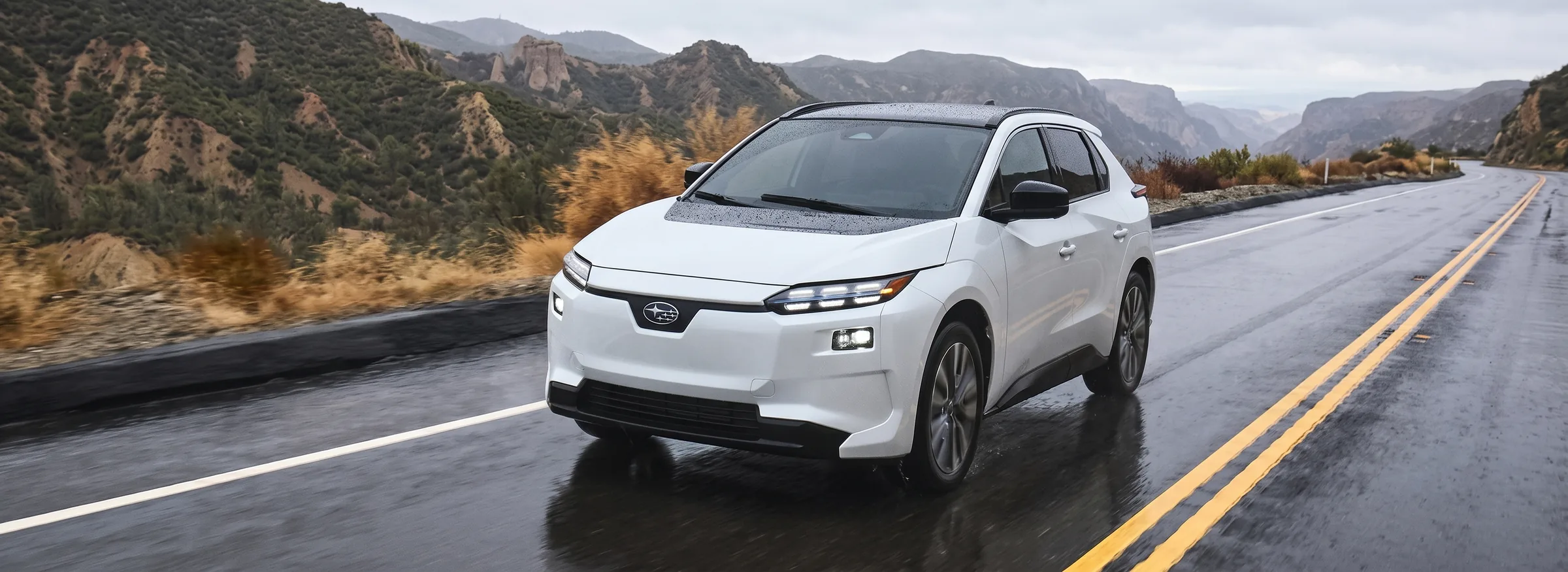 A white 2026 Subaru Solterra driving on a wet mountain highway