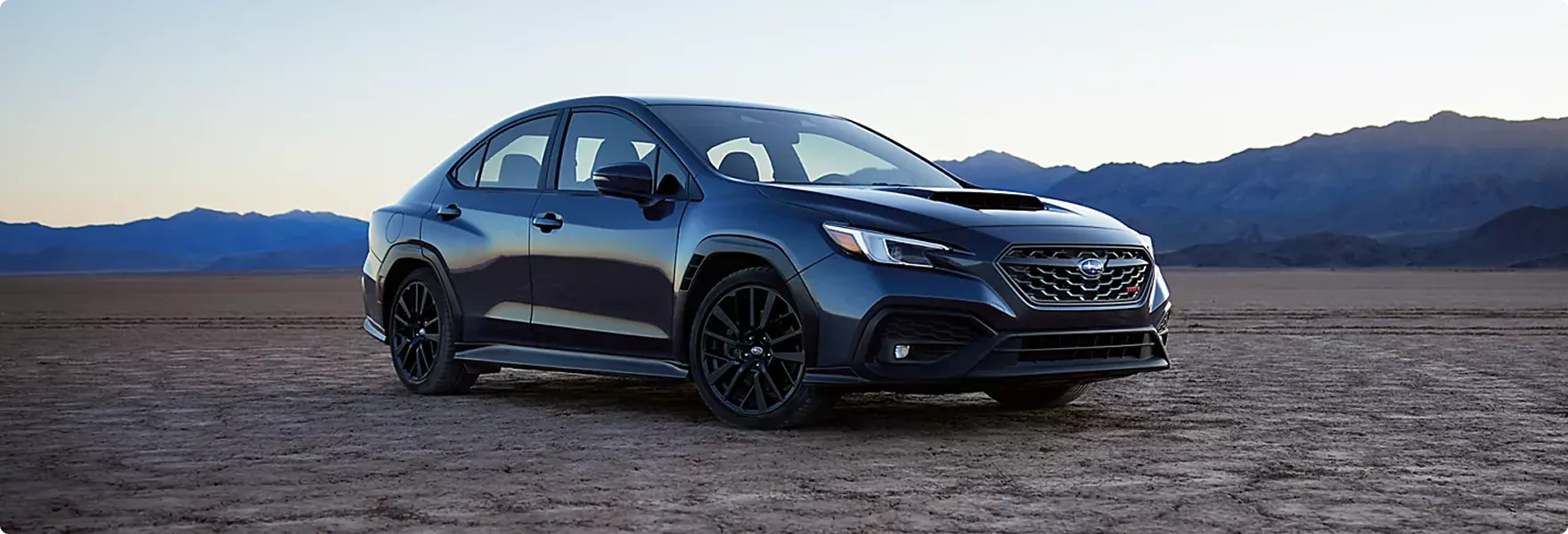 A dark Subaru WRX GT parked against a mountain skyline