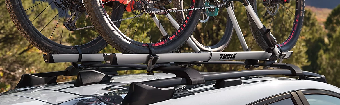 Two mountain bikes mounted on the roof rack of a Subaru Crosstrek in a forest