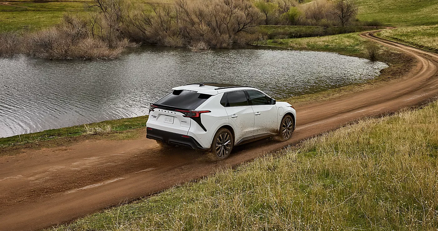 A white 2026 Subaru Solterra on a dirt road beside a pond