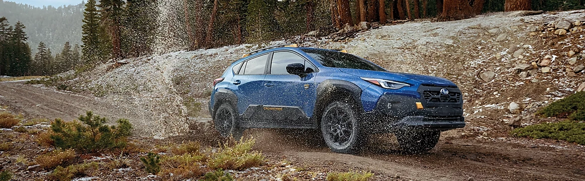 A blue Subaru Crosstrek splashing through a shallow creek crossing on a rocky trail