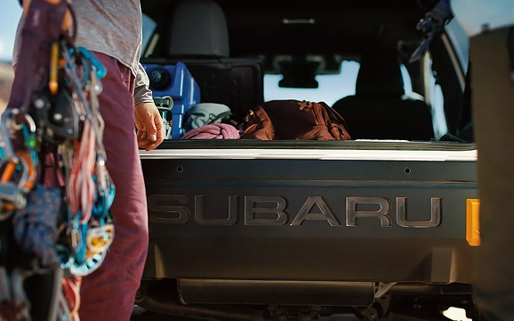 A climber wearing carabiners standing at the open rear gate of a Subaru Crosstrek