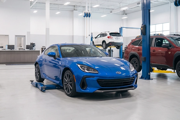 A blue Subaru BRZ on a low-rise jack in the Baldwin Subaru workshop, with a Forester and a red Outback raised on lifts behind it