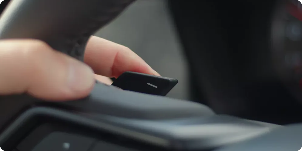 A hand reaching for the steering-wheel paddle shifter in the WRX