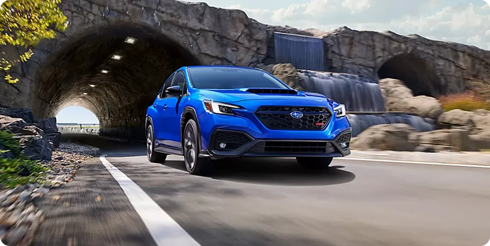 A blue Subaru WRX tS emerging from a tunnel on a mountain pass