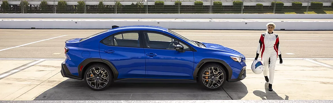 A blue Subaru WRX with a driver standing alongside on a track