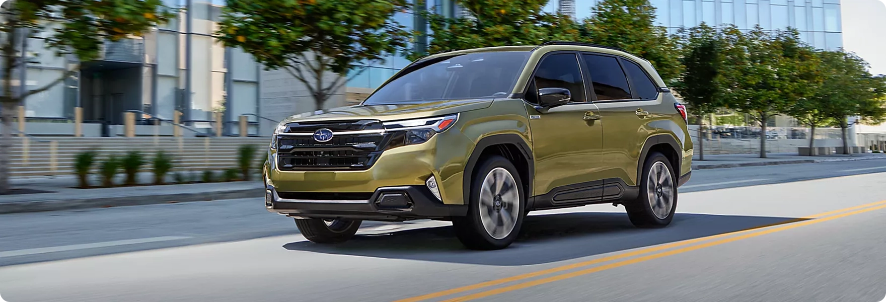 A gold-green 2026 Subaru Forester driving past a modern glass office building
