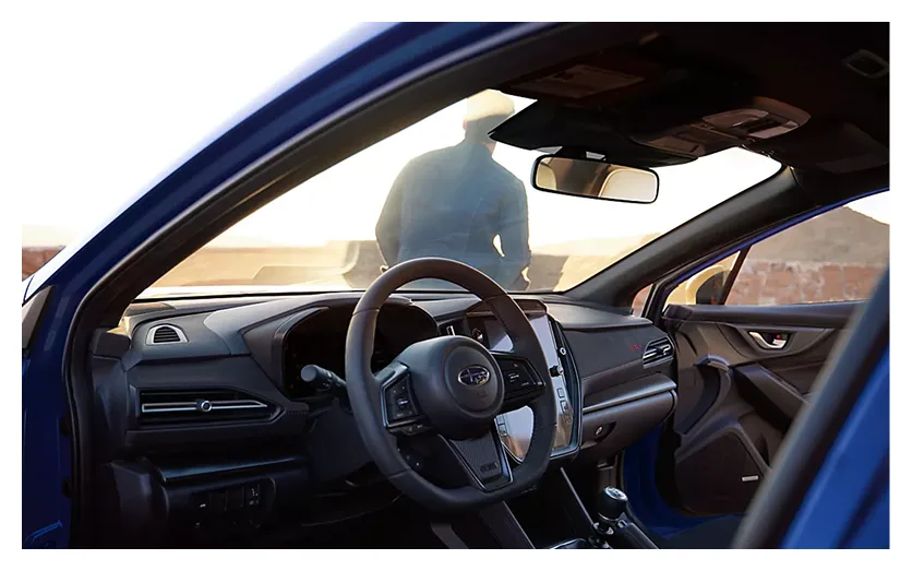 Driver at the D-shaped WRX steering wheel seen through the open door