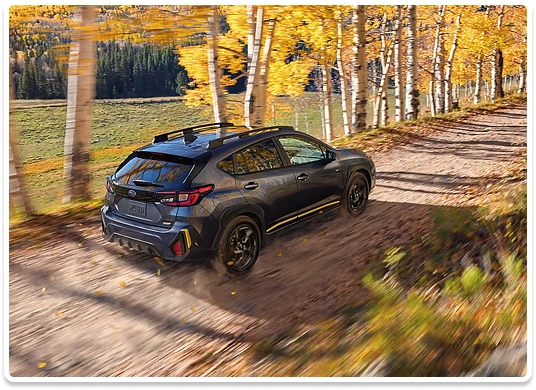 A dark gray Subaru Crosstrek Sport driving a dirt track through golden autumn aspens