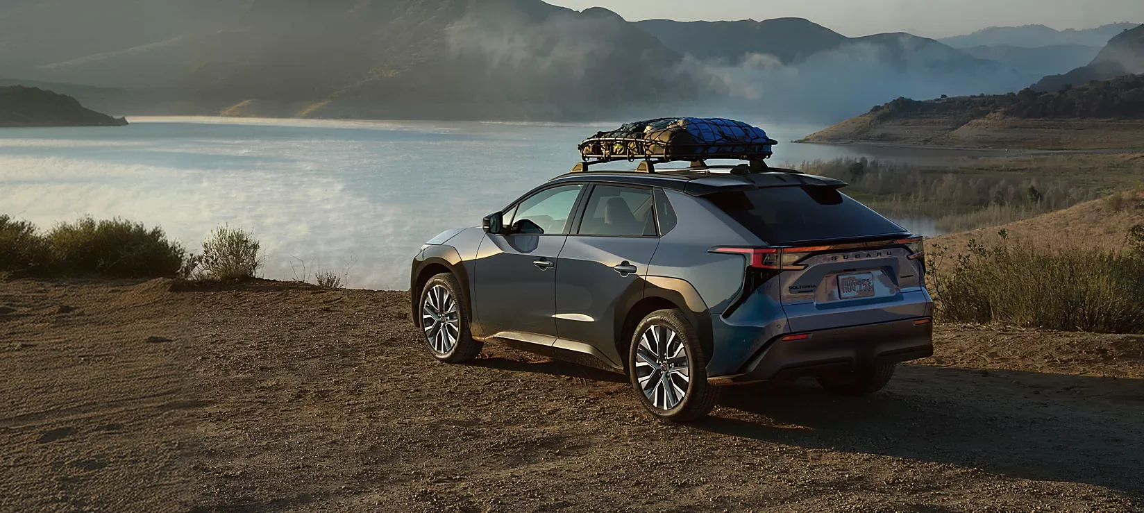 A dark 2026 Subaru Solterra carrying roof-mounted gear on a lakeside trail at dusk