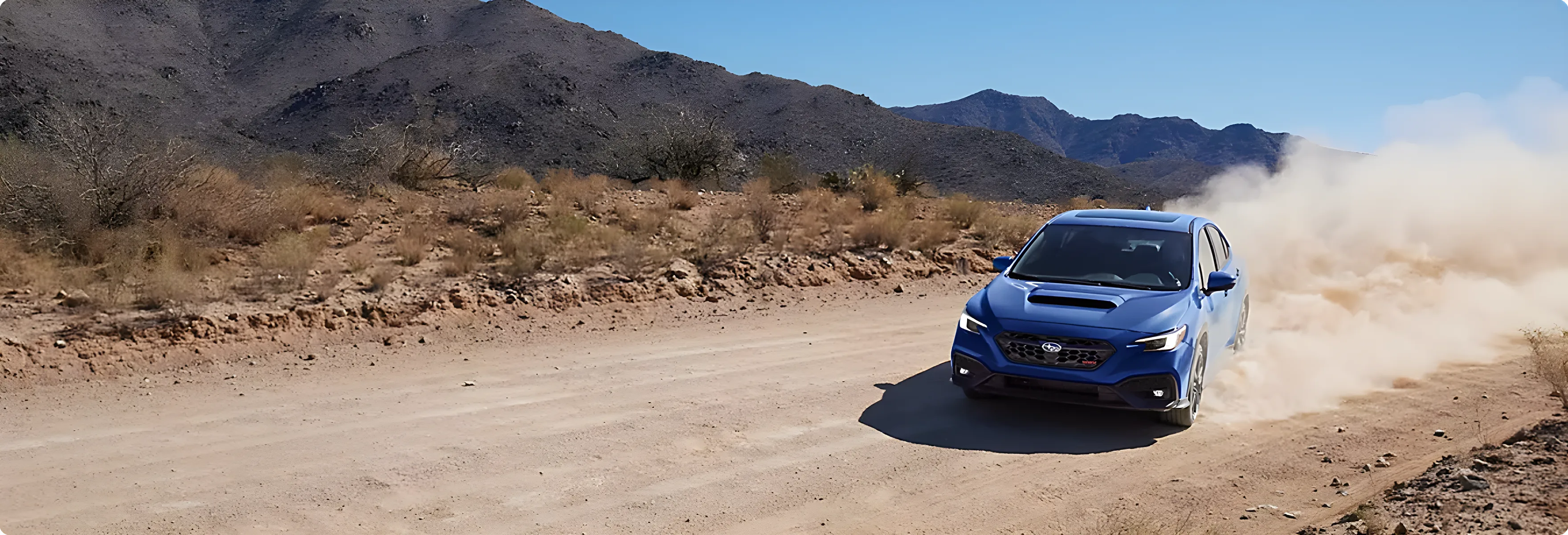 A blue Subaru WRX on a dirt road with mountains behind