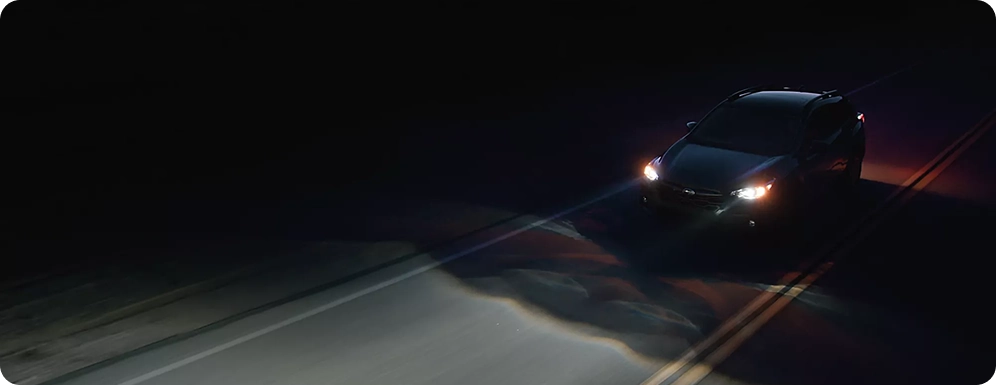 A Subaru with its headlights illuminating a dark country road at night