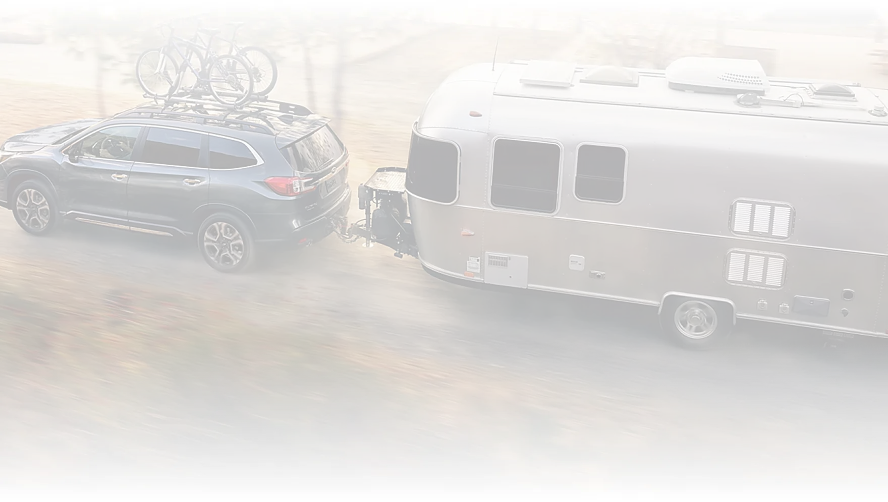 A Subaru Ascent towing a silver travel trailer along a winding country road