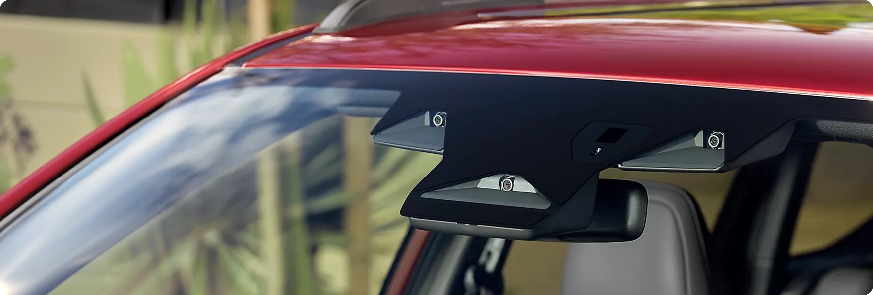 A close-up of the EyeSight dual-camera unit mounted beside the rearview mirror of a red Subaru Forester