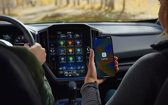 A passenger holding a smartphone beside the Apple CarPlay screen in a Subaru Crosstrek
