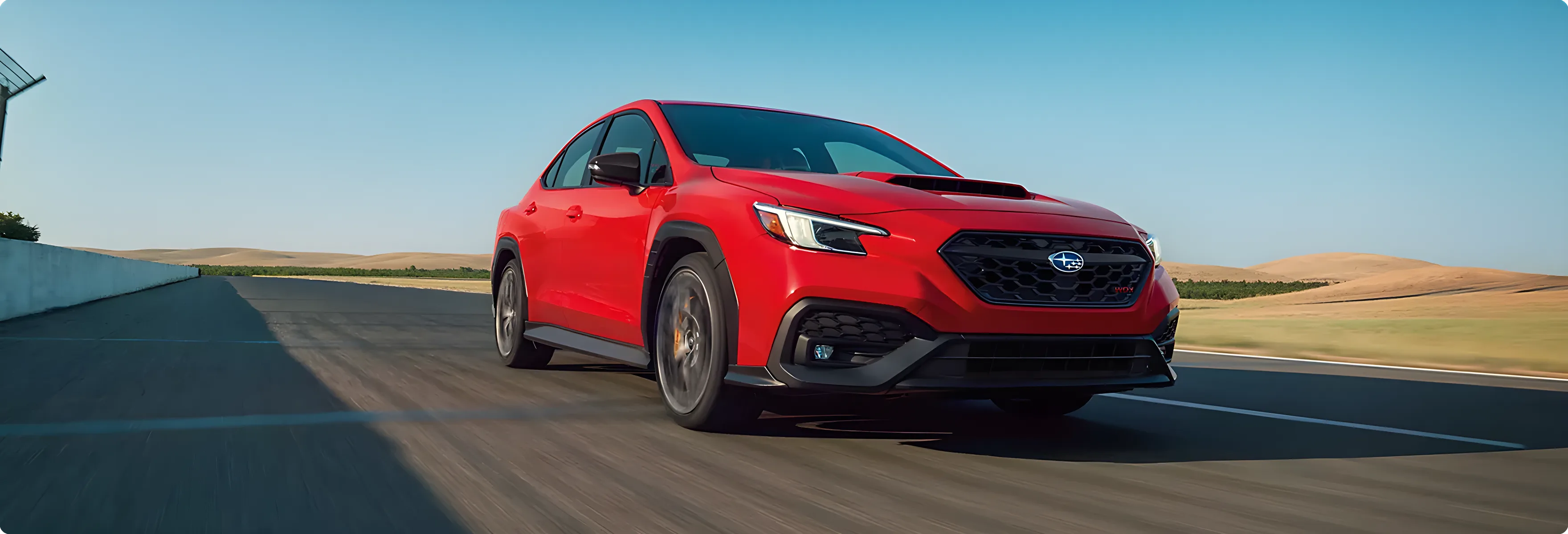 A red Subaru WRX tS on a coastal road at speed