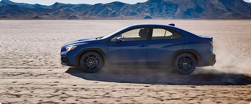 A blue Subaru WRX on a desert flat with mountains behind
