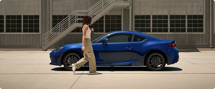 A blue Subaru BRZ parked in a covered walkway as a person passes