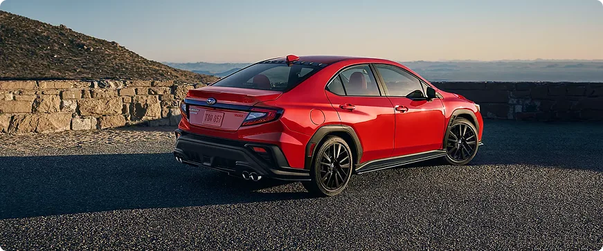 Rear three-quarter view of a red Subaru WRX beside a stone wall